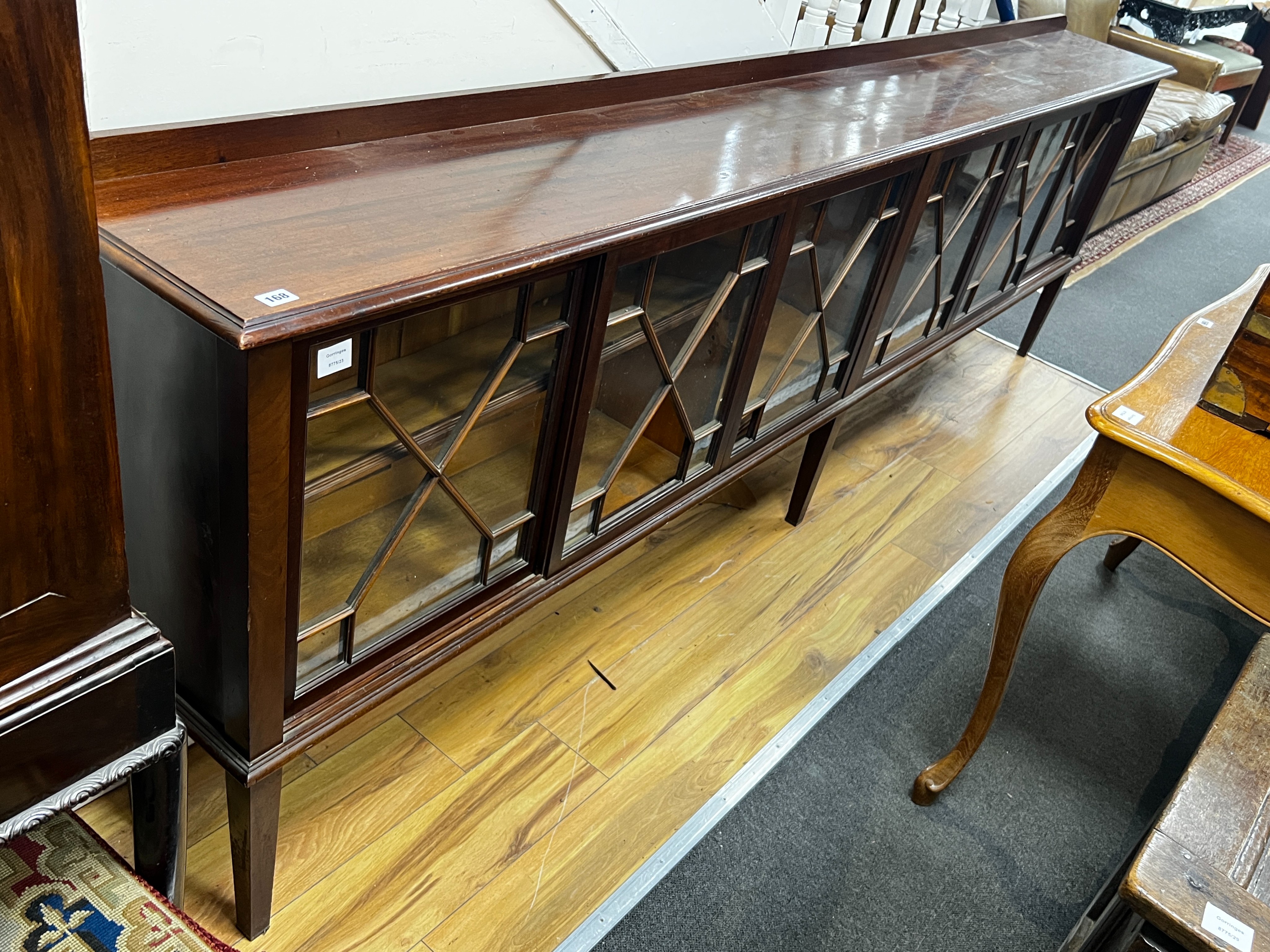 An Edwardian glazed mahogany dwarf bookcase, enclosed by six astragal glazed sliding doors, width 290cm, depth 34cm, height 94cm